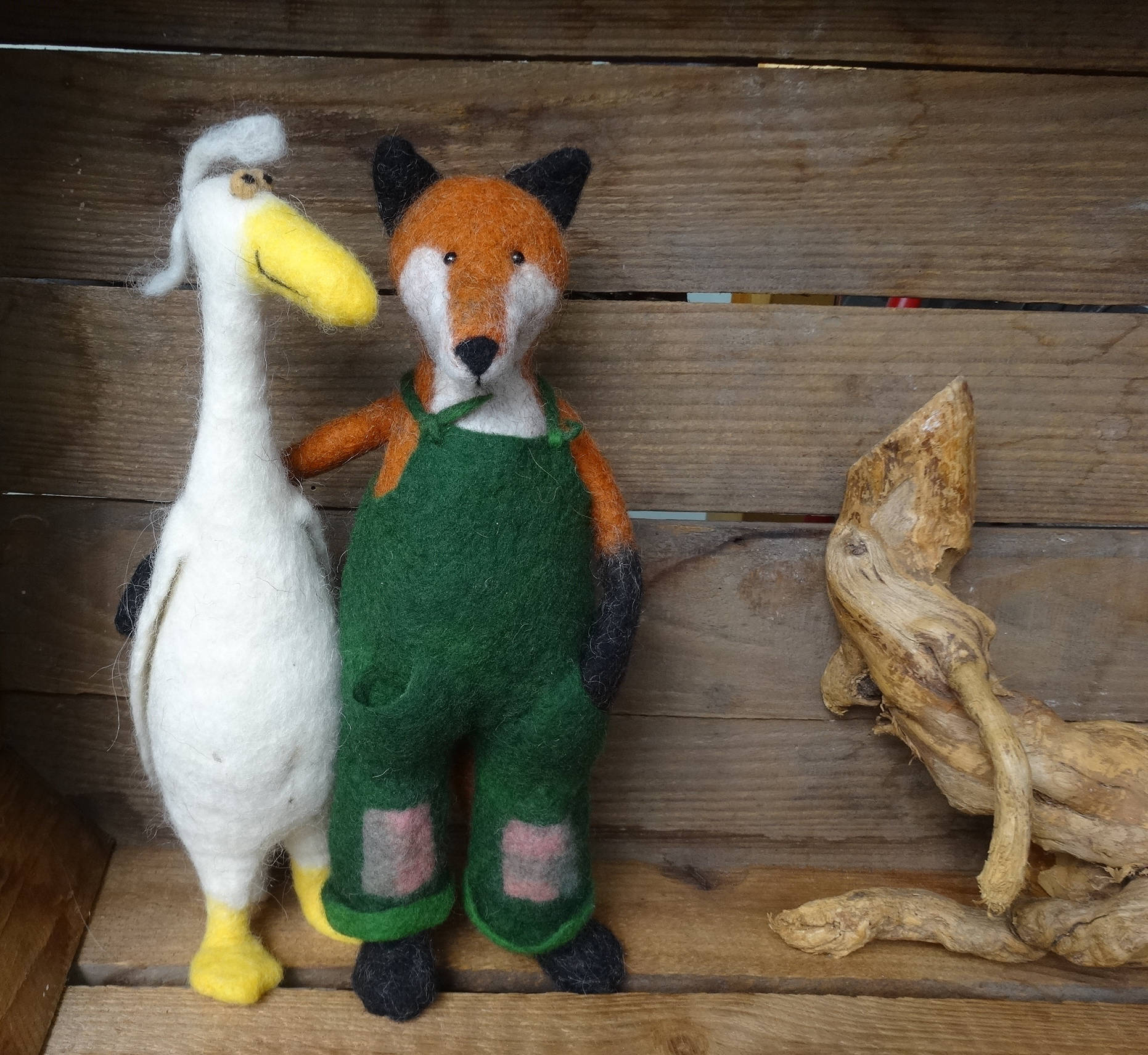 Ein gefilzter Fuchs mit grüner  Latzhose hält eine weiße gefilzte Gans im Arm