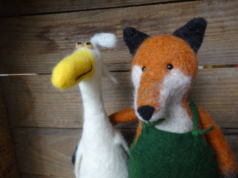 Ein gefilzter Fuchs mit grüner Latzhose neben einer weißen, gefilzten Gans.