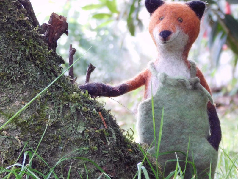 Gefilzter Fuchs in grüner Latzhose neben Baum